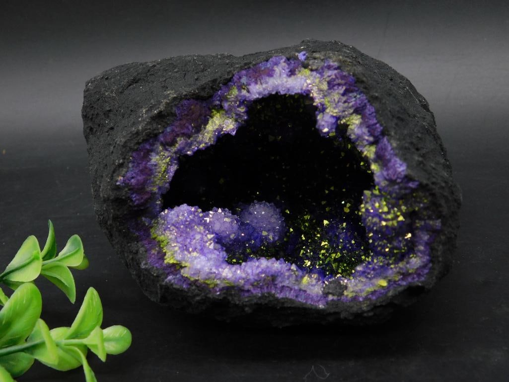 Purple and Gold Geode Rock Stone Lapidary Specimen Cluster: This is a stunning amethyst geode with a deep black outer surface and a cavernous interior featuring purple crystal formations. Accentuated with green and yellowish hues, the crystal formations shine 