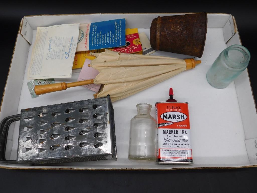Assorted Household Items Including Ink, Grater, and Umbrella: This lot includes assorted household items: a used grater, a vintage-style cream-colored umbrella, a small brown-handled can, a clear glass jar, a tin of Marsh T-Grade Marker Ink, old documents, and m