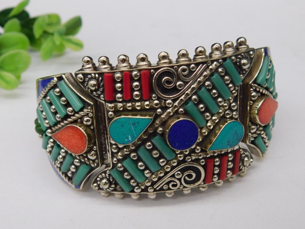 Turquoise, Lapis Lazuli, and Red Coral Metal Bracelet with Inlay Design: Decorative bracelet featuring a raised metalwork pattern with colorful inlay elements in turquoise, red, orange, and blue tones. Hinged design with an integrated clasp for secure closure. Appears to b