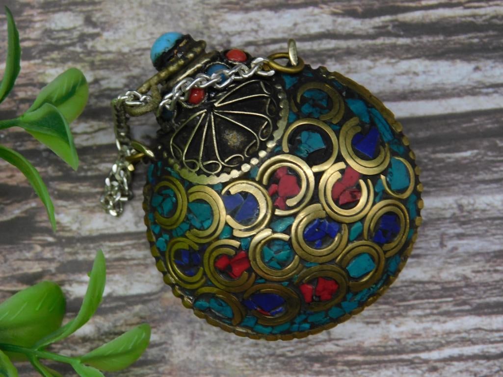Multicolor Inlaid Snuff Bottle with Decorative Design: Decorative multicolor ornament featuring inlaid design in red, blue, and turquoise hues. Gold-toned metal casing with intricate circular patterns. Small chain attached at the top along with a miniatur