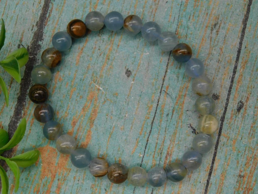 Polished Beaded Bracelet in Earth Tones: This is a polished bracelet made with round beads featuring earthy tones of blue, green, and brown. The bracelet is elastic, allowing it to stretch for a comfortable fit. The beads present slight vari