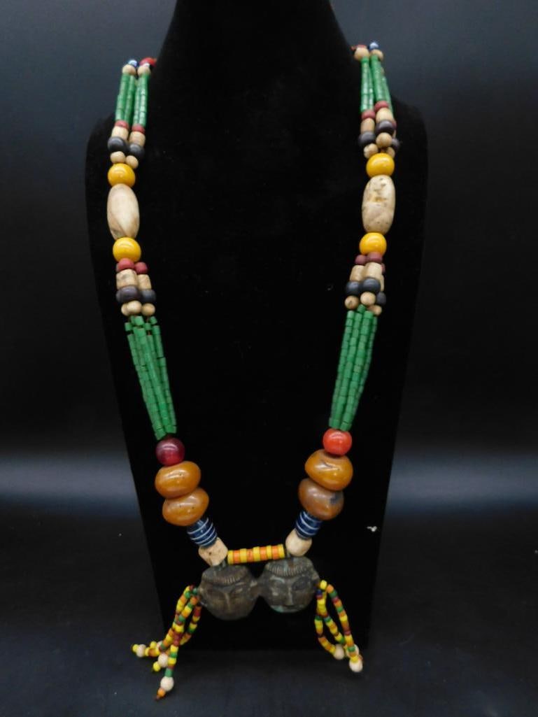 African Trade Beads Multicolored Tribal Necklace With Double Head Pendant: A tribal-style necklace featuring a variety of colorful beads, including green, yellow, blue, red, and amber tones. The centerpiece consists of a double-headed pendant with multicolored bead tassels.