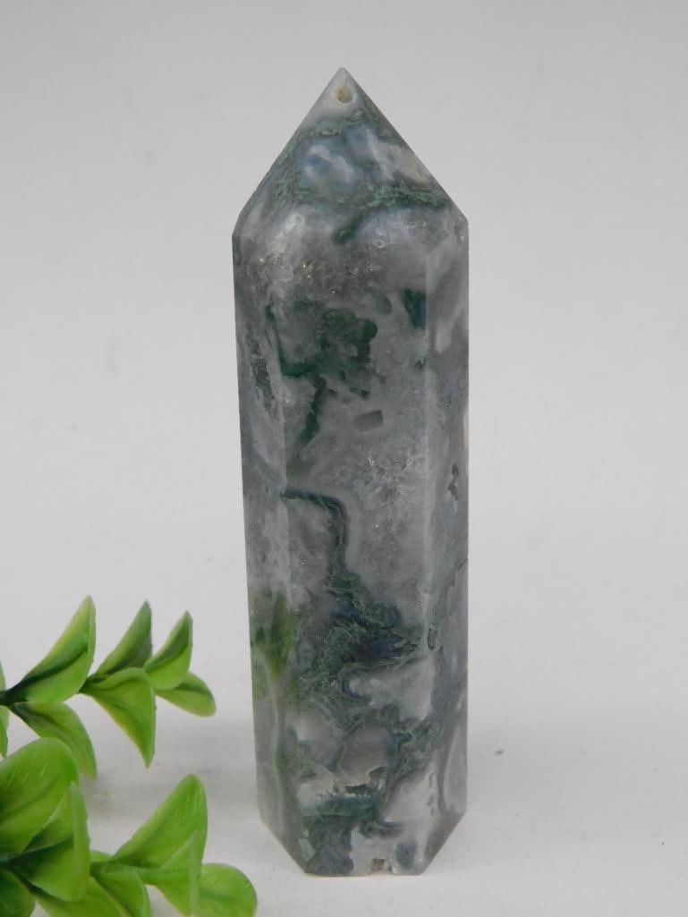Moss Agate Point Tower Rock Stone Lapidary Specimen: Polished green moss agate crystal point showcasing natural moss-like inclusions. Features one pointed end and one flat end for balanced placement. Weighs 99 grams as noted on the tag. Rustic yet appea