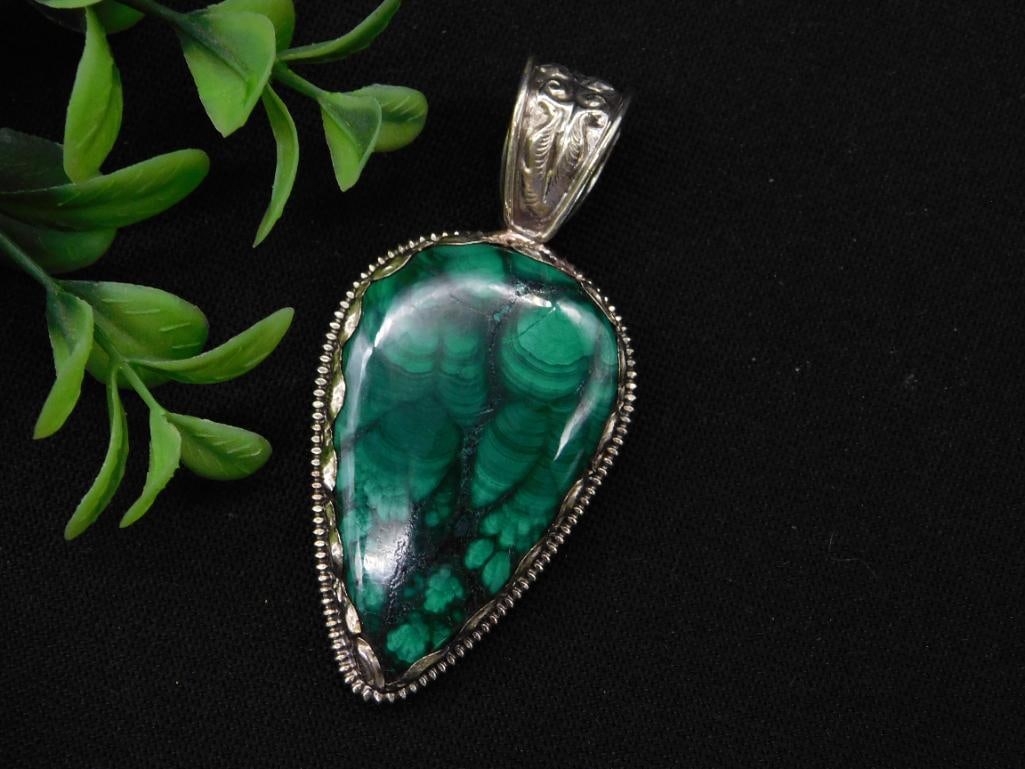 Malachite Pendant with Decorative Bail ROCK STONE LAPIDARY SPECIMEN: This pendant features a teardrop-shaped malachite stone. The detailed bezel and decorative bail add a distinct design element. The reverse side showcases intricate silverwork with a floral pattern. A