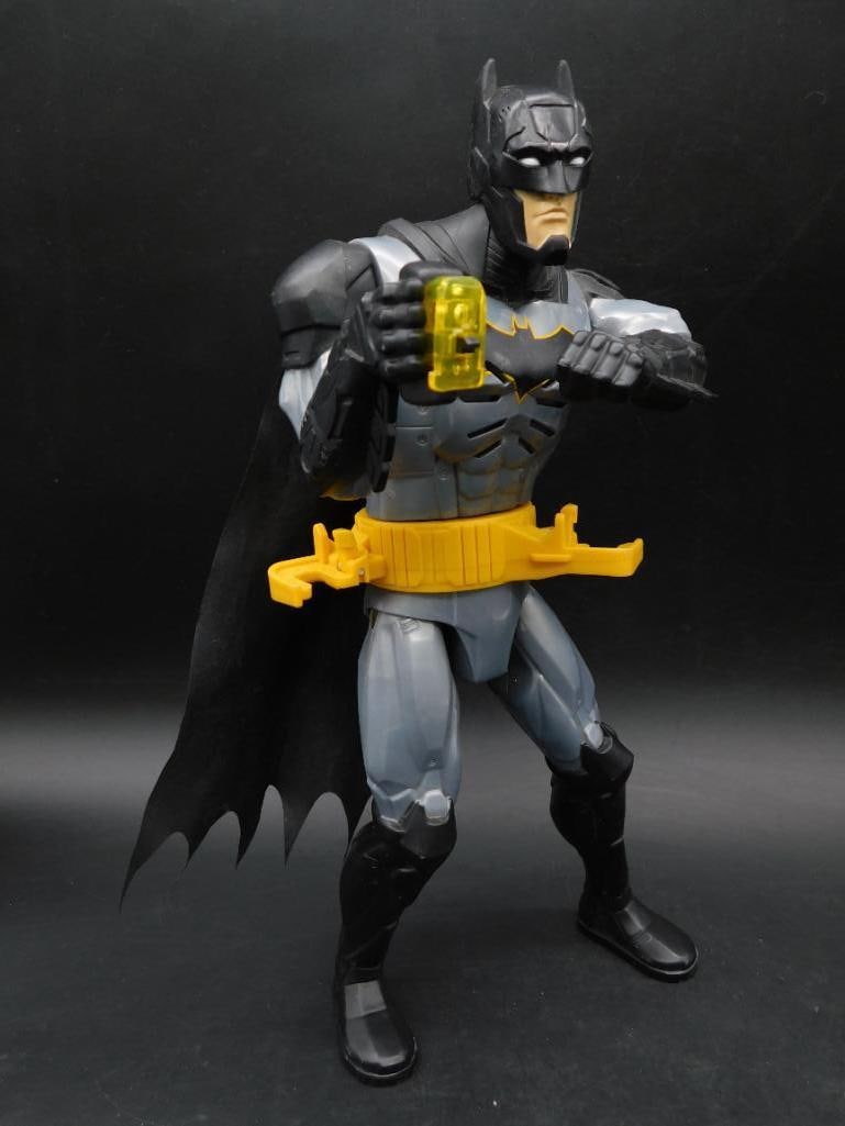 Batman Action Figure With Yellow Utility Belt: Batman action figure featuring a gray and black costume with a yellow utility belt. Includes a yellow weapon accessory in one hand and mechanical components visible beneath the belt. Markings on the f