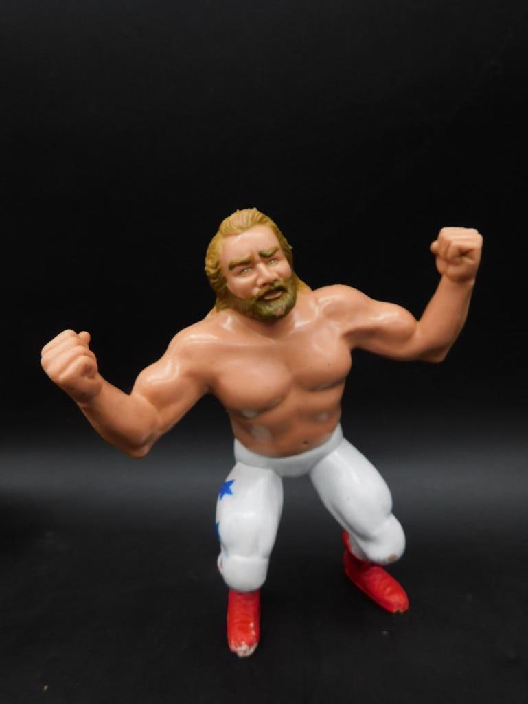 1986 Titan Sports Wrestling Action Figure: This 1986 Titan Sports wrestling action figure features a muscular pose with blonde hair, white pants with blue star details, and red boots. The marking on the back confirms its authenticity as a lice