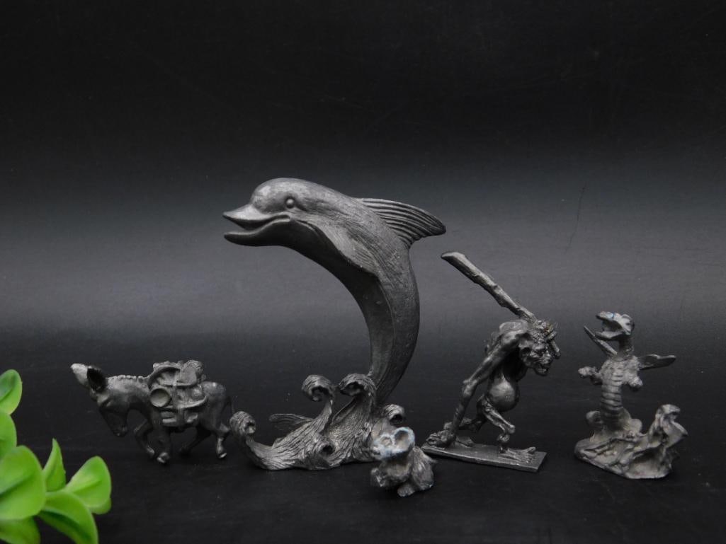 Collection of Pewter Figurines Including Dolphin and Creatures: This lot features a collection of intricately crafted pewter figurines. Included are a leaping dolphin on waves, several animal figures, and a unique humanoid figure with a club. The base of one figur