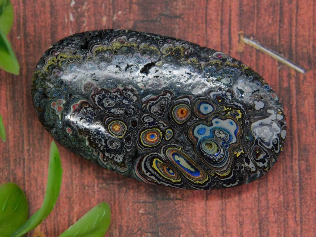 FORDITE MOTOR CITY AGATE CABOCHON ROCK STONE LAPIDARY SPECIMEN: - Attractive oval-shaped cabochon with vibrant, multicolored patterns across the surface. | - Composed of layered materials creating intricate, swirling designs. | - High-polish finish enhances visibi