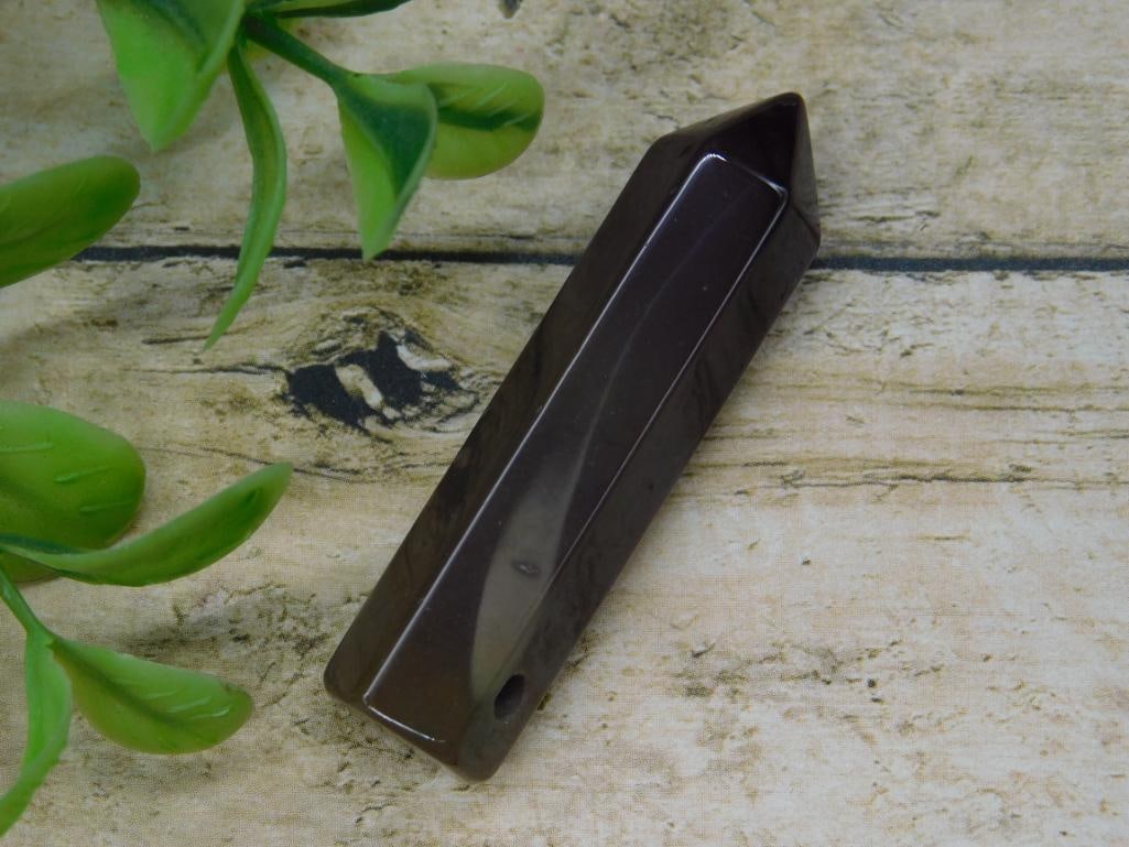 Polished Stone Point ROCK STONE LAPIDARY SPECIMEN: Polished stone point featuring a sleek finish and a drilled hole near one end. The point is dark in color and appears to be made of solid material. A coin is included in the image to showcase scale, a