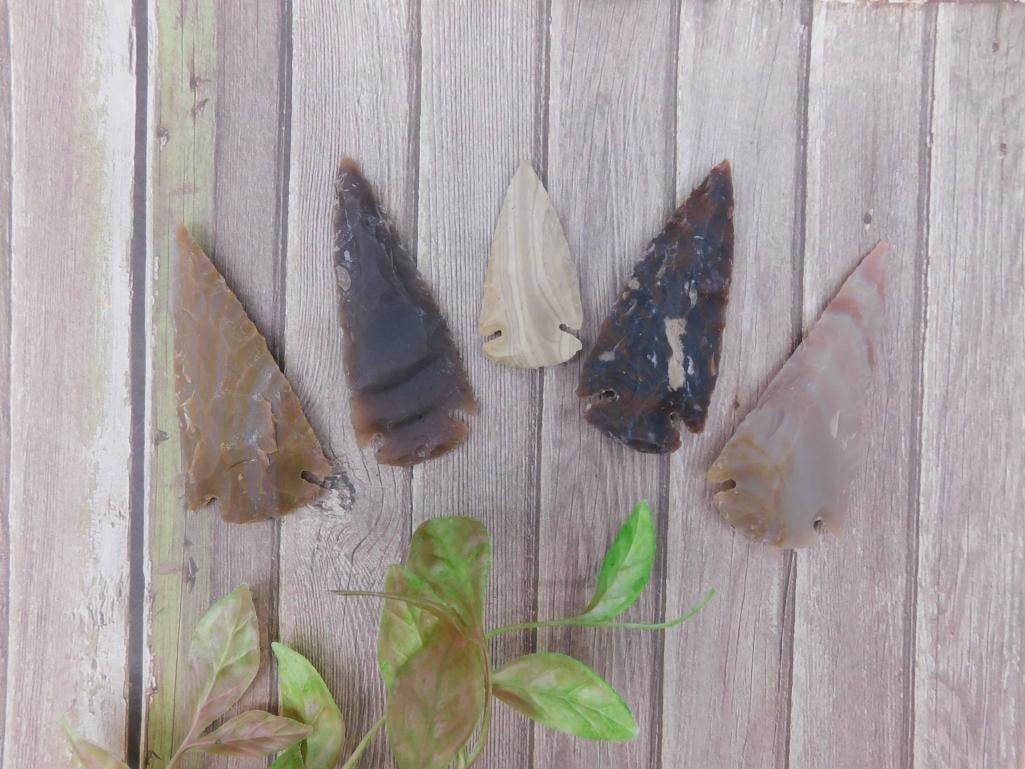 Set of Five Stone Arrowheads ROCK STONE LAPIDARY SPECIMEN: This lot includes five stone arrowheads of varying colors and textures. Each piece has drilled holes, allowing for varied display or use. The items are presented with a ruler in the image, showing app