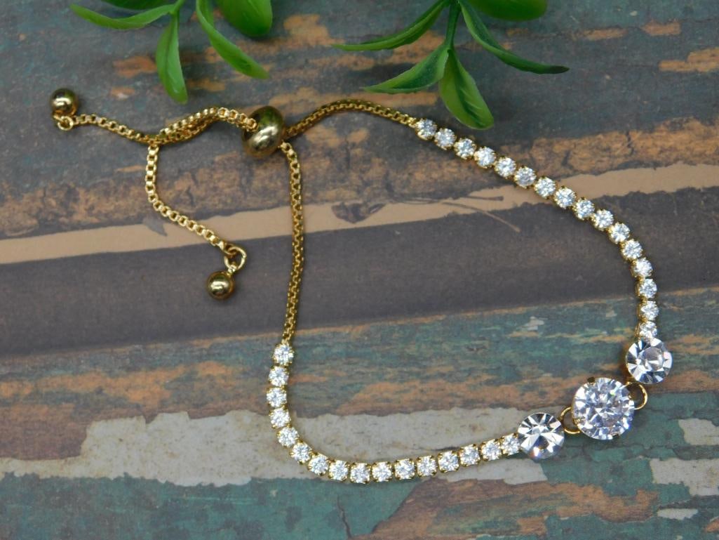Gold-Tone Adjustable Bracelet with Clear Stones: Gold-tone adjustable bracelet featuring clear round-cut stones. Bracelet has a sliding bead clasp for an adjustable fit. Prominent design includes three larger central stones flanked by smaller stones