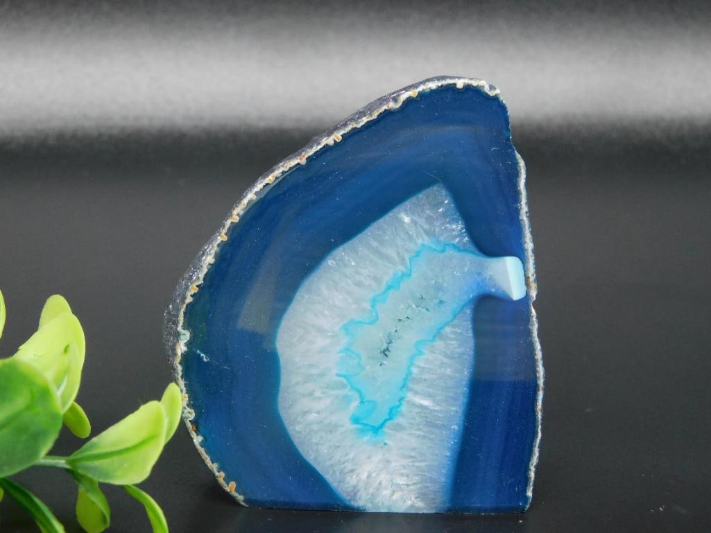 Blue Agate Rock Stone Lapidary Specimen: - Blue agate geode slice with a striking natural pattern featuring vibrant blue and white hues. | - Polished finish on one side enhances the geode's translucent properties. | - Weighs approximately 20