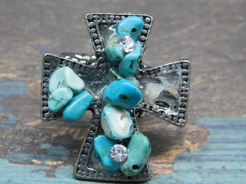 Turquoise and Rhinestone Cross Ring with Stretch Band: - Cross-shaped ring design featuring turquoise stones and rhinestones. | - Stretchy band allows for adjustable sizing. | - Made with metal elements and uniquely arranged stones. | - Approximate size i