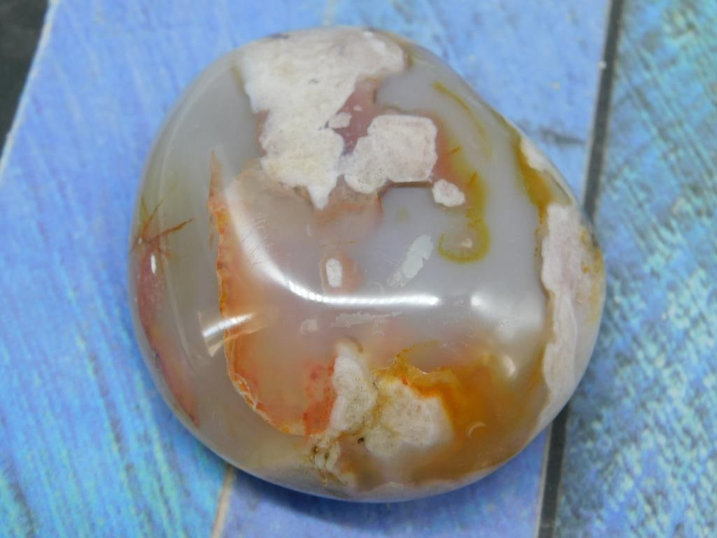 Hatmans Flower Petal Agate Rock Stone Lapidary Specimen: - Polished agate stone showcasing natural multicolor patterns, including hues of orange, white, yellow, and translucent areas. - Approximate weight of 113 grams, as indicated. - Smooth surface with an