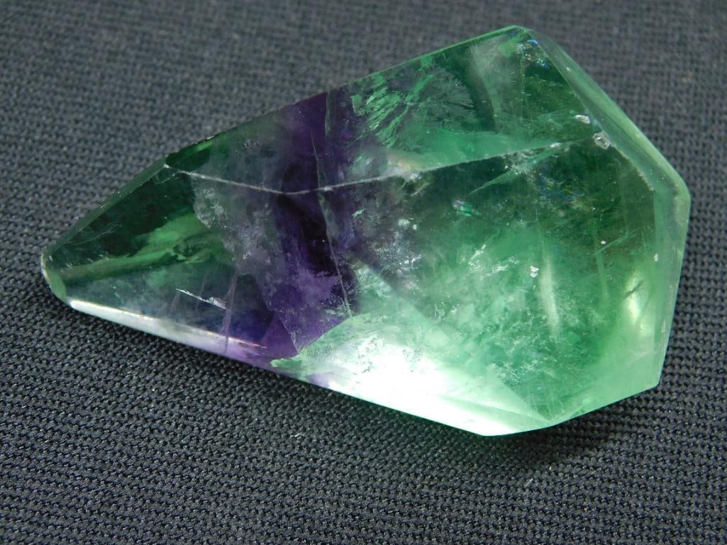 Faceted Green and Purple Fluorite Gemstone Rock Stone Lapidary Specimen: - A faceted fluorite gemstone with green and purple hues. | - Approximate weight: 71 grams as shown. | - Displayed next to a ruler and a coin for scale reference. | - Suitable for collectors, enthusia