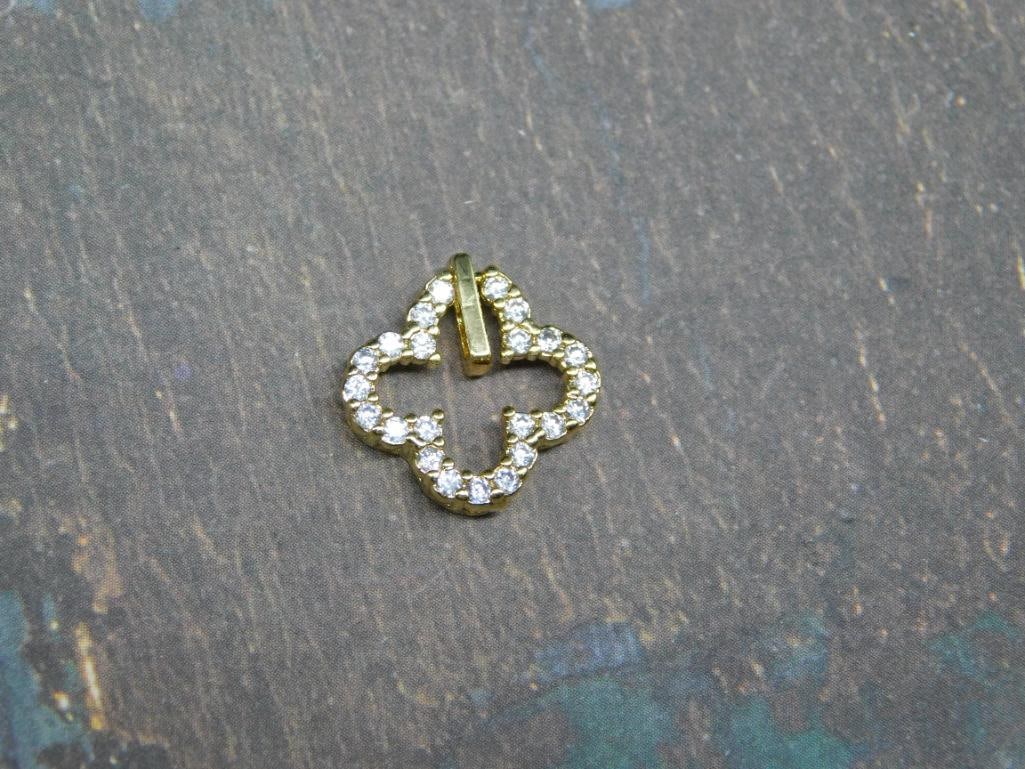 Gold-Tone Clover Pendant with Clear Stones: - Clover-shaped pendant adorned with clear, round-cut stones | - Gold-tone metal for an elegant appearance | - Small size, as shown next to a US dime for scale | - Suitable for necklaces or bracelets 