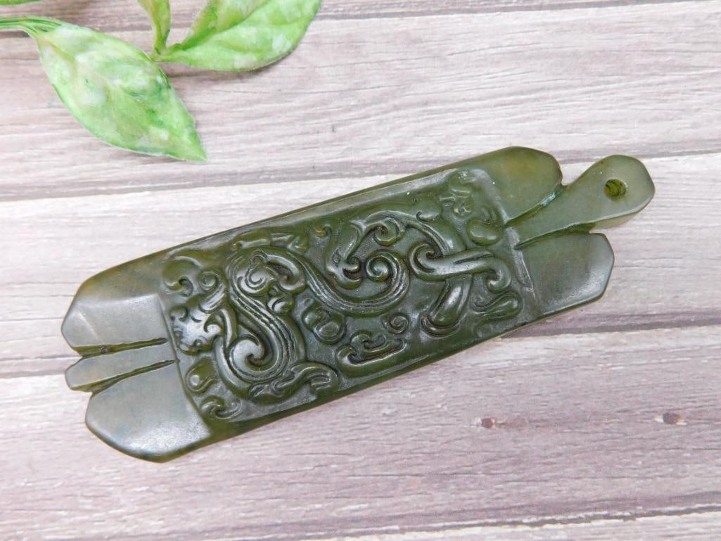 Carved Green Jade Pendant With Ornamental Design: This is a carved green stone pendant featuring a decorative design on one side and a feather-like carving on the reverse. The pendant includes a hole for attaching a cord or chain. It weighs approxima