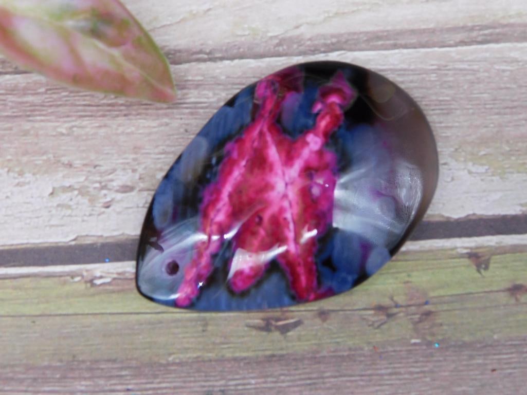 Polished Teardrop-Shaped Gemstone Pendant: Polished teardrop-shaped gemstone pendant featuring dynamic shades of pink and blue on a dark background. Includes a drilled hole for easy mounting or attachment. Measures approximately 1.5 inches acr