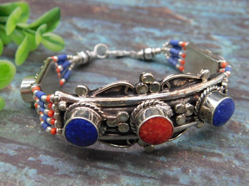 Metal Beaded Bracelet With Lapis Lazuli and Red Coral Accents: Silver-tone bracelet featuring intricate decorative metalwork and beadwork. Incorporates red and blue stone details with colorful bead patterns. Measures approximately 7 inches in length (see ruler fo