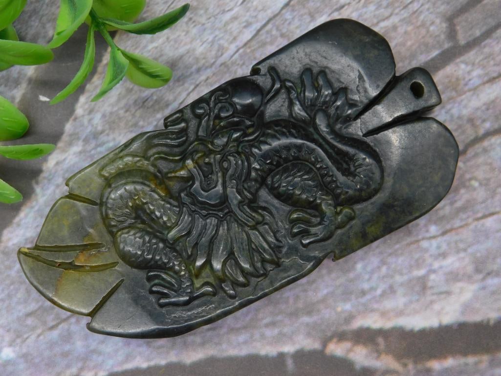 Handcrafted Jade Pendant With Dragon Design: This is a handcrafted jade pendant featuring a detailed dragon design. The piece appears carved from a dark jade material, with a hole at the top for stringing or hanging. It weighs 70 grams, as indic