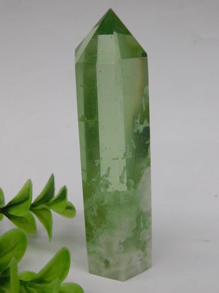 Green Crystal Tower With Polished Point: Green crystal wand with a polished hexagonal point and flat base. Weighs approximately 70 grams. Features green and white tones within the crystal, with visible natural inclusions. Ideal for collector