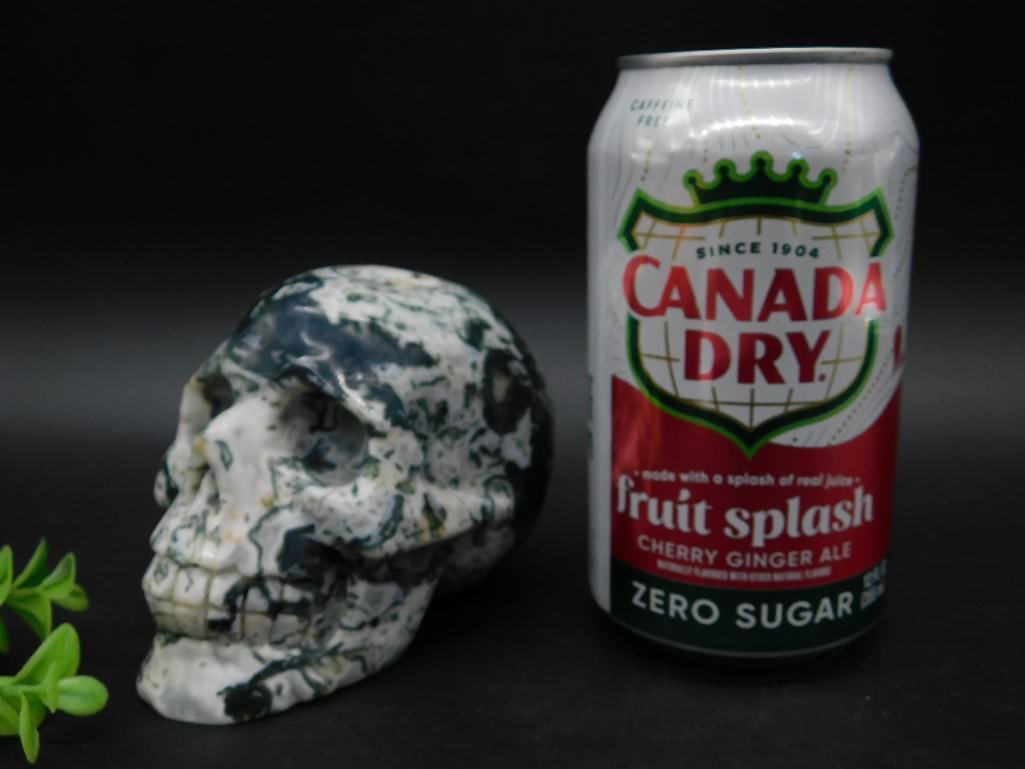MOSS PLUME LARGE STONE SKULL ROCK STONE LAPIDARY SPECIMEN: Green and white stone sculpture carved in a skull design. Features a natural marbled pattern. Material, weight, and details presented alongside a can and ruler for size reference. Ideal for collectors