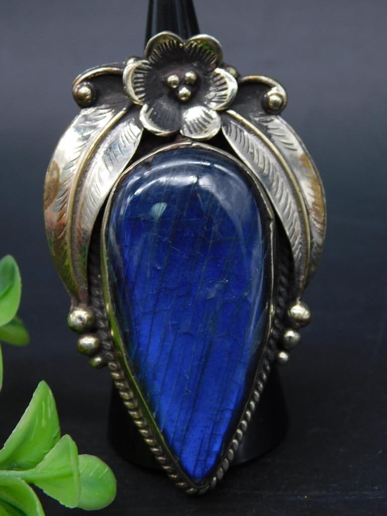 Adjustable Labradorite Statement Ring with Intricate Tooling: Beautiful silver ring featuring a large, teardrop-shaped blue labradorite stone. The ring is accented with floral and leaf-inspired silverwork. The back of the ring includes intricate silver engraving