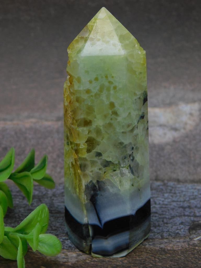 Polished Green and Black Crystal Point Wand: This listing features a polished crystal point with green, yellow, and black coloration. The piece weighs 96 grams and is designed with a pointed tip and smooth edges. It showcases natural textures, b