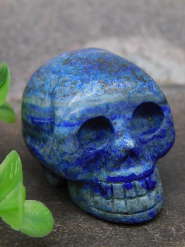 Blue Lapis Lazuli Carved Skull, 48 Grams: A carved skull made from blue Lapis Lazuli, weighing 48 grams. Features detailed carved features and vibrant blue tones with natural patterning variations in the stone. Includes auction tag as seen in