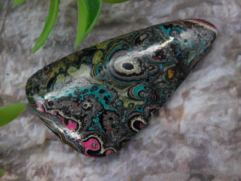 Polished Fordite Motor City Agate Slice with Multicolor Swirl Pattern: Polished agate slice featuring a unique multicolor swirl pattern. The stone exhibits a mix of vibrant hues, including teal, magenta, and black. The piece is approximately quadrilateral in shape, shown