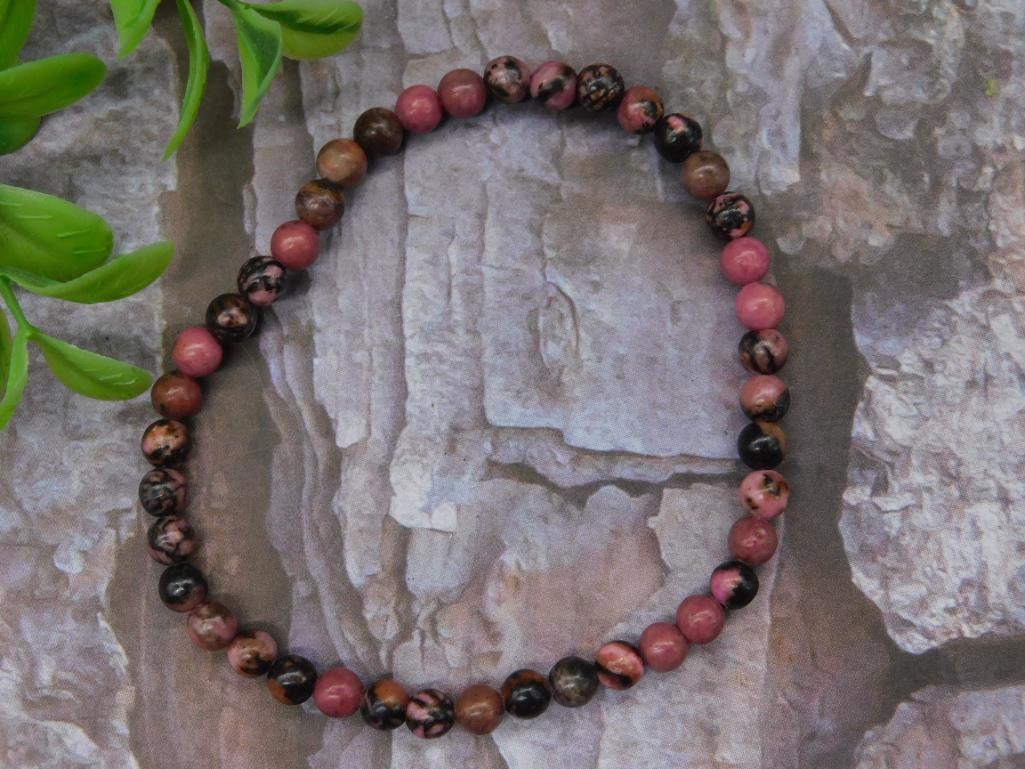 Rhodonite Stone Beaded Bracelet: Pink and brown stone beaded bracelet featuring round beads evenly strung on an elastic band. Includes a variety of natural tones and patterns. Measures approximately 7 inches unstretched, based on com