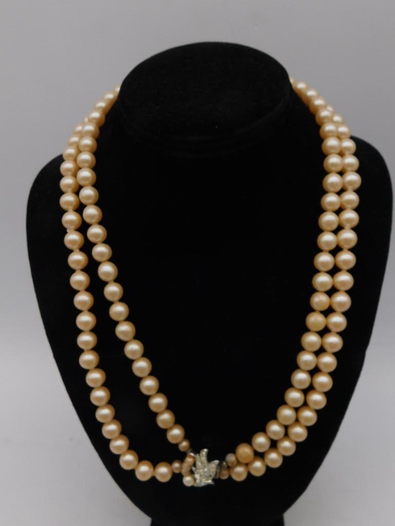 Double-Strand Pearl Necklace With Rhinestone Clasp: - Double-strand pearl necklace with cream-colored pearls. | - Features an ornate rhinestone clasp in a floral or abstract design. | - Necklace length roughly 24 inches as per the included measurement.