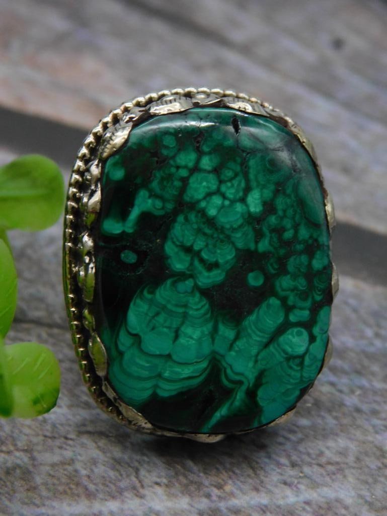 Vintage Malachite Ring with Ornate Setting Rock Stone Lapidary Specimen: - Features a polished malachite stone with vibrant green and dark green patterns. | - Set in an ornate silver-toned adjustable band with decorative detailing. | - Oval-shaped stone and ring back show