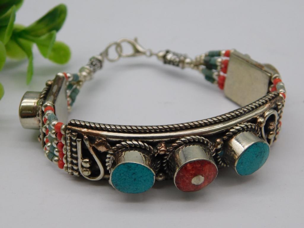 Silver Bracelet with Turquoise and Red Coral Accents: - Features a silver-tone base with intricate design embellishments. | - Adorned with turquoise and red coral decorative stones in circular settings. | - Includes red and green beaded accents along bot