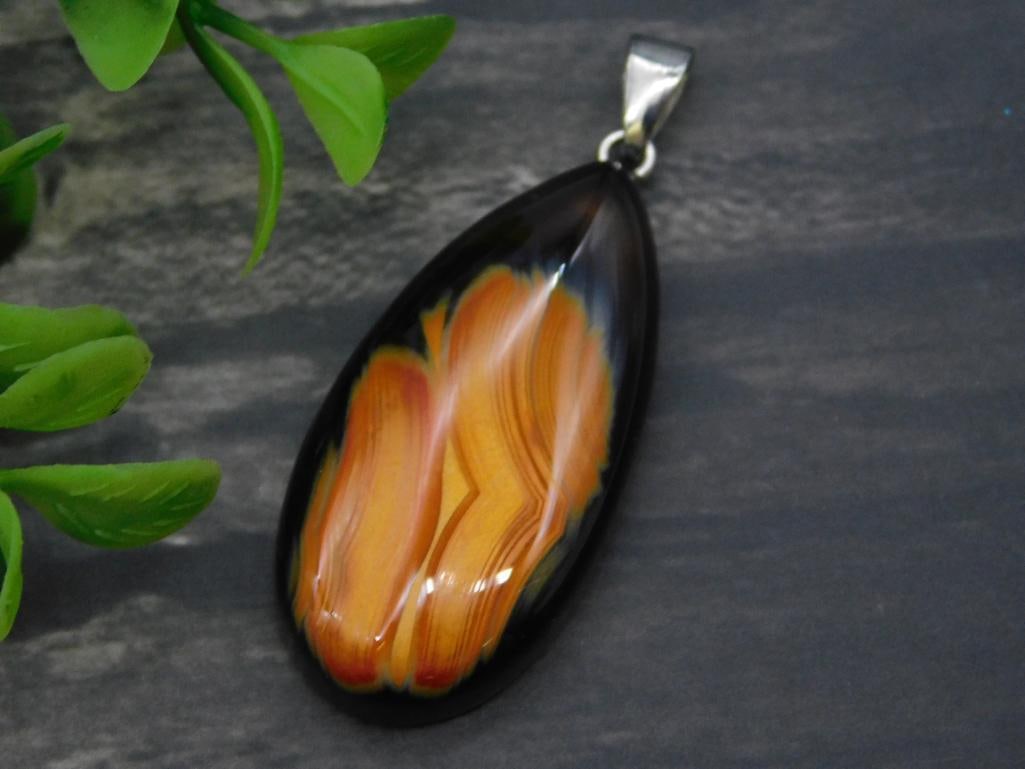 Eclipse Agate Pendant Rock Stone Lapidary Specimen: - Glass pendant featuring a floral design in orange and yellow hues. | - Smooth oval shape with a polished finish. | - Silver-colored bail suitable for chains or cords. | - Dimensions not specified; s