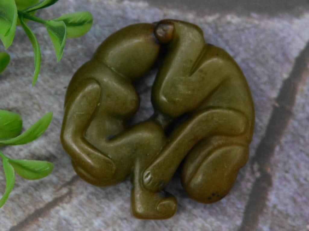 Carved Jade Figurine of Intertwined Forms Rock Stone Lapidary Specimen: - Carved stone figurine depicting two intertwined human-like forms. | - Crafted from green-hued stone with a smooth finish. | - Compact size as shown compared to a U.S. quarter for scale. | - Intrigui