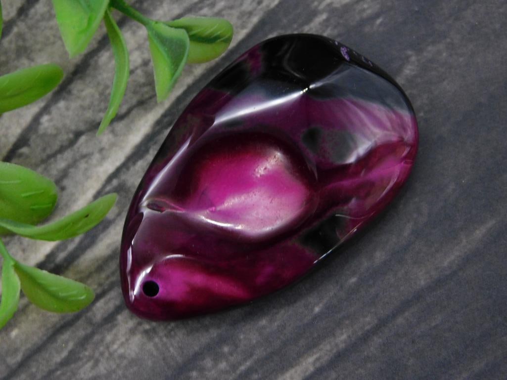 Fuchsia and Black Stone Pendant With Drilled Hole: - Natural stone pendant featuring vibrant fuchsia and black coloration. | - Smoothly polished surface with a unique abstract shape. | - Single drilled hole at the top, suitable for stringing or hangin