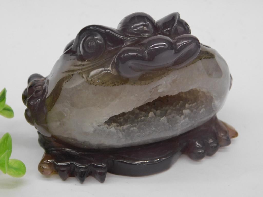Carved Crystal Frog Figurine With Geode Detail Rock Stone Lapidary Specimen: - Figurine depicting a frog carved from crystal material. | - Features a natural geode cavity on the underside, showcasing clear crystalline formations. | - Dark polished exterior with fine detailing 