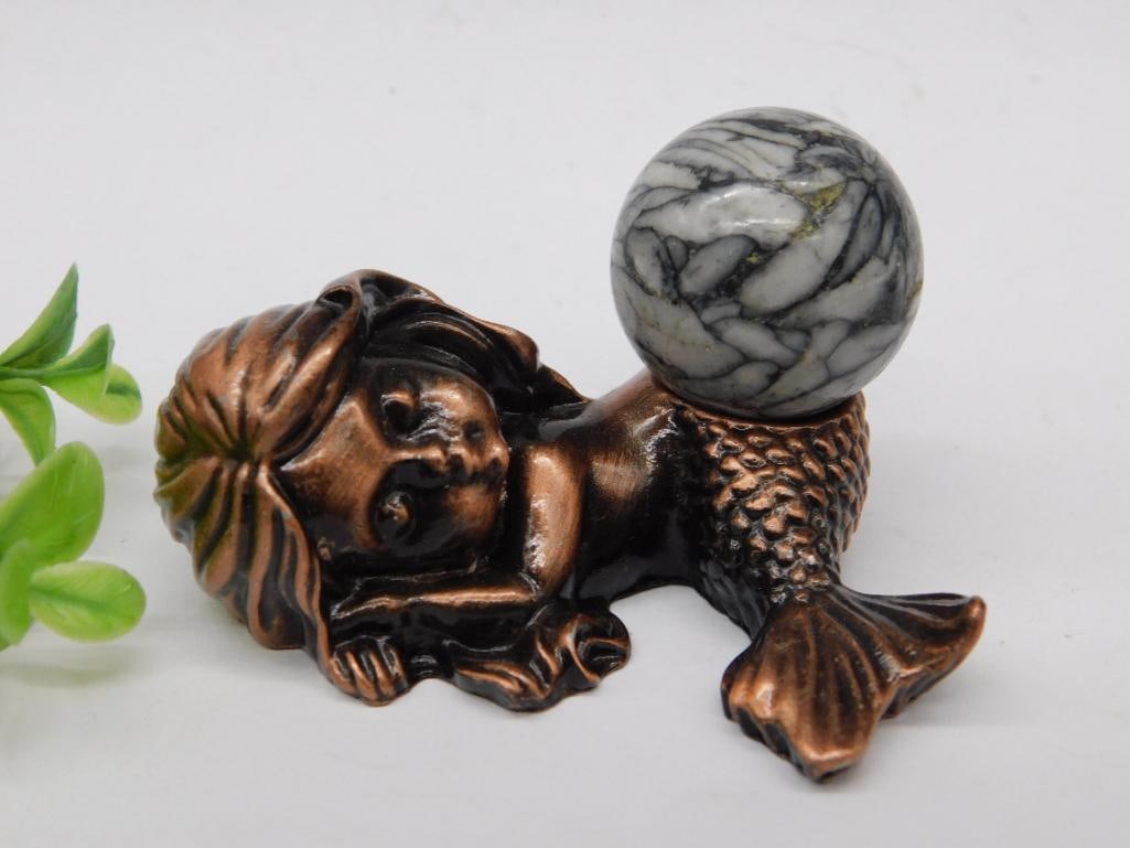 Bronze Mermaid Figurine with Pinolith Sphere Rock Stone Lapidary Specimen: - Bronze-like mermaid figurine crafted with intricate details. | - Mermaid design incorporates a textured tail and delicate facial features. | - Accompanied by a marble-like sphere with a black and wh