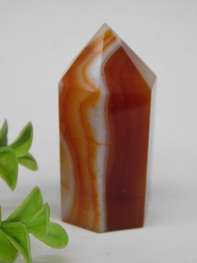 Banded Carnelian Tower Rock Stone Lapidary Specimen: - Polished gemstone tower showcasing vibrant red and white banded patterns. | - Crafted in a pointed, faceted shape for display or collection. | - Approximate weight: 62 grams. | - Smooth finish highl