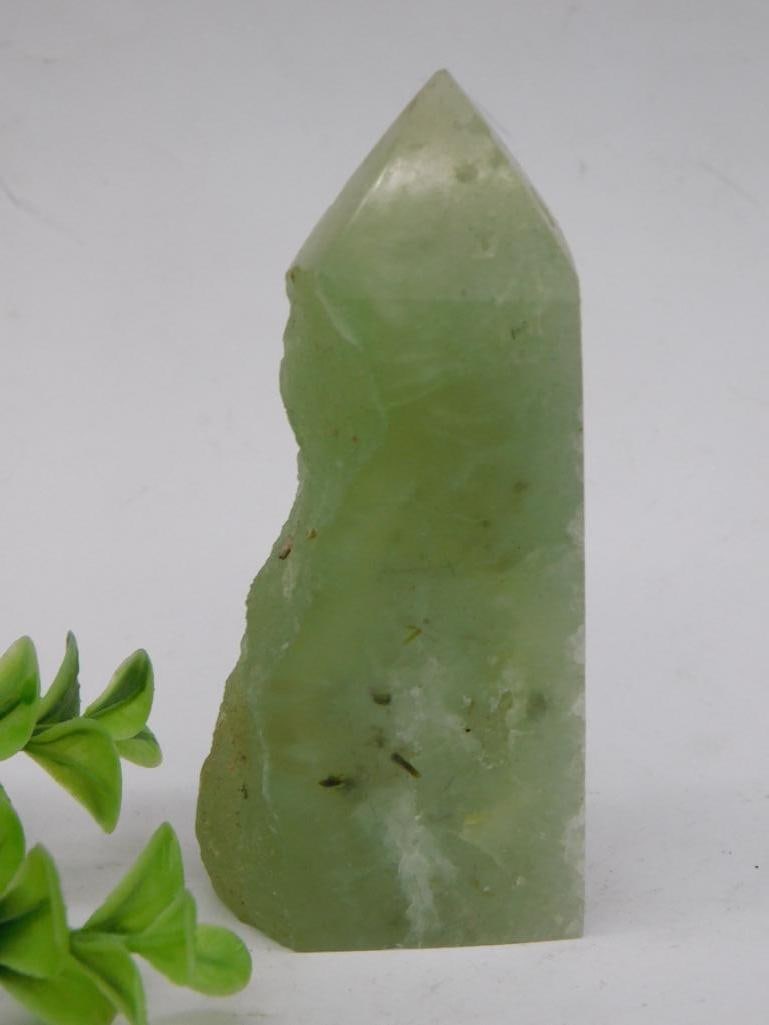 Prehnite Tower Rock Stone Lapidary Specimen: - Natural green quartz crystal point cut with smooth and polished surfaces. | - Displays a translucent green hue with irregular natural inclusions. | - Shaped into a pointed cylindrical form with one