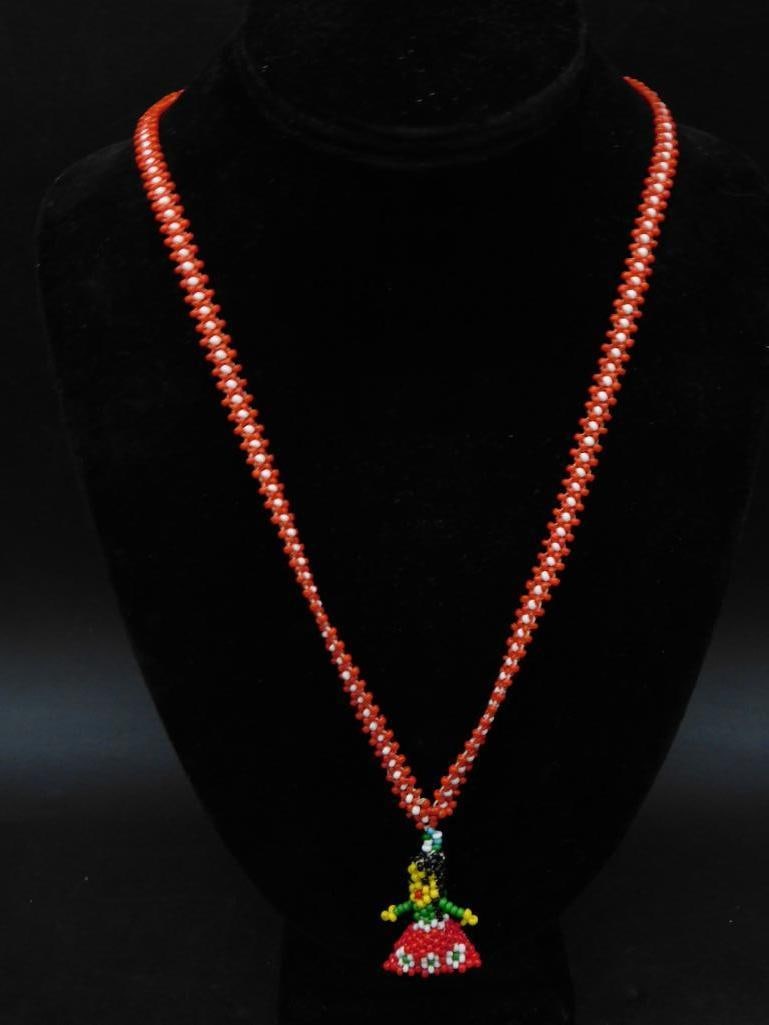 Handcrafted Beaded Necklace with Figure Pendant: - Vibrantly colored handcrafted beadwork necklace. | - Red beaded chain with white accents. | - Pendant features a colorful figure design crafted with precision beads. | - Combination of yellow, green