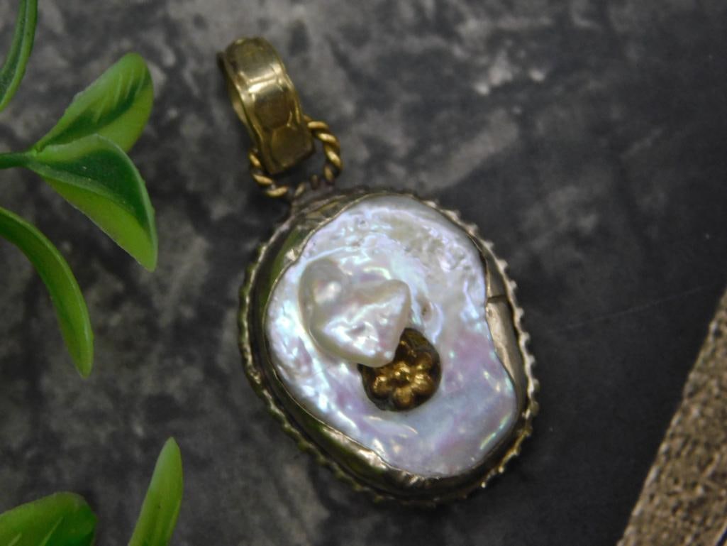 Vintage Baroque Pearl and Metal Pendant with Gold-Toned Details: - Ornate pendant featuring a natural pearl centerpiece. | - Gold-toned metal accents, including a twisted detail around the edge. | - Back of the pendant features intricate metalwork. | - Includes a b