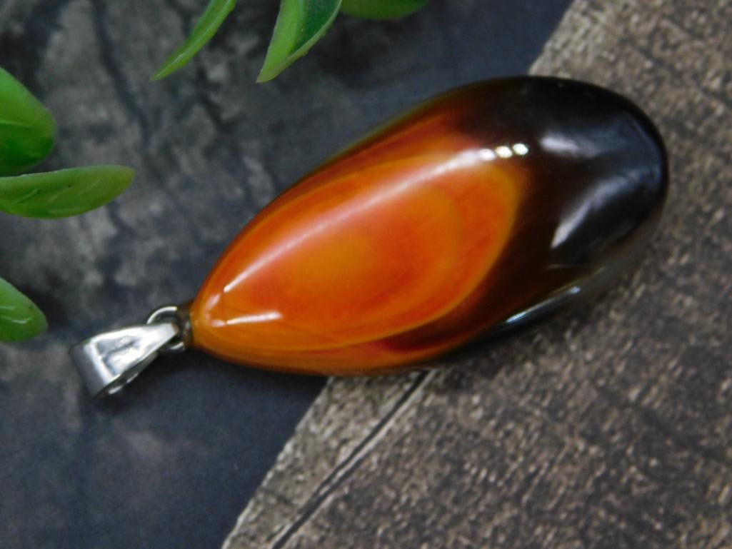 Eclipse Agate Pendant Rock Stone Lapidary Specimen: - Teardrop-shaped polished agate stone pendant with vibrant orange and black hues. | - Includes a silver-toned metal bail for easy attachment to chains or cords. | - Approximate dimensions visible in