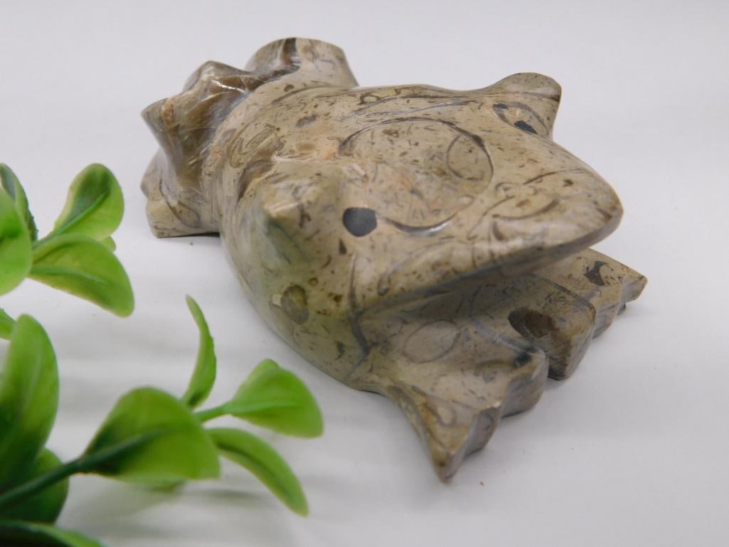 Hand-Carved Stone Frog Rock Stone Lapidary Specimen: - Hand-carved stone figurine crafted in the shape of a frog. | - Made from an earthy-tone polished stone material with natural patterns and markings. | - Dimensions relative to a quarter shown for sca