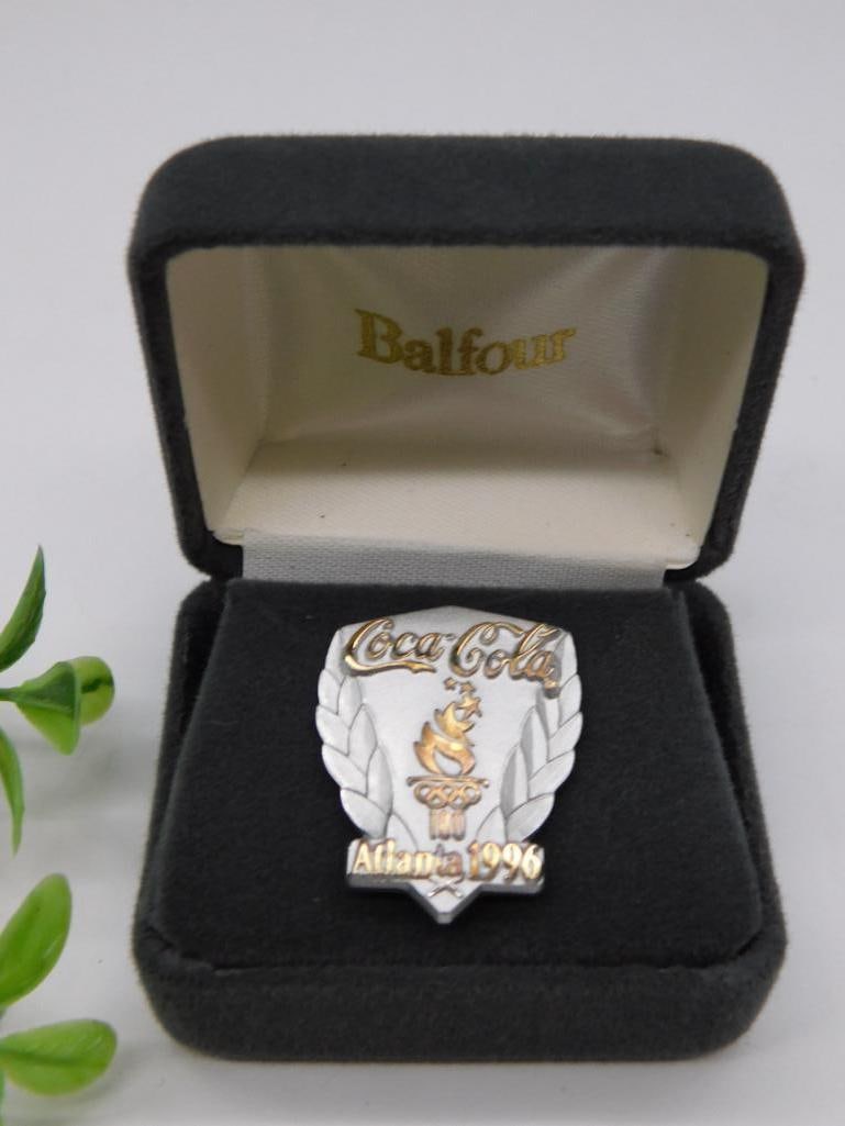 Limited Edition 1996 Coca-Cola Shield Pin with COA: - Commemorative Coca-Cola shield pin created for the 1996 Atlanta Olympic Games. | - Features "Coca-Cola" branding and gold-toned details with a laurel leaf design. | - Marked as "1162 of 5000," indic
