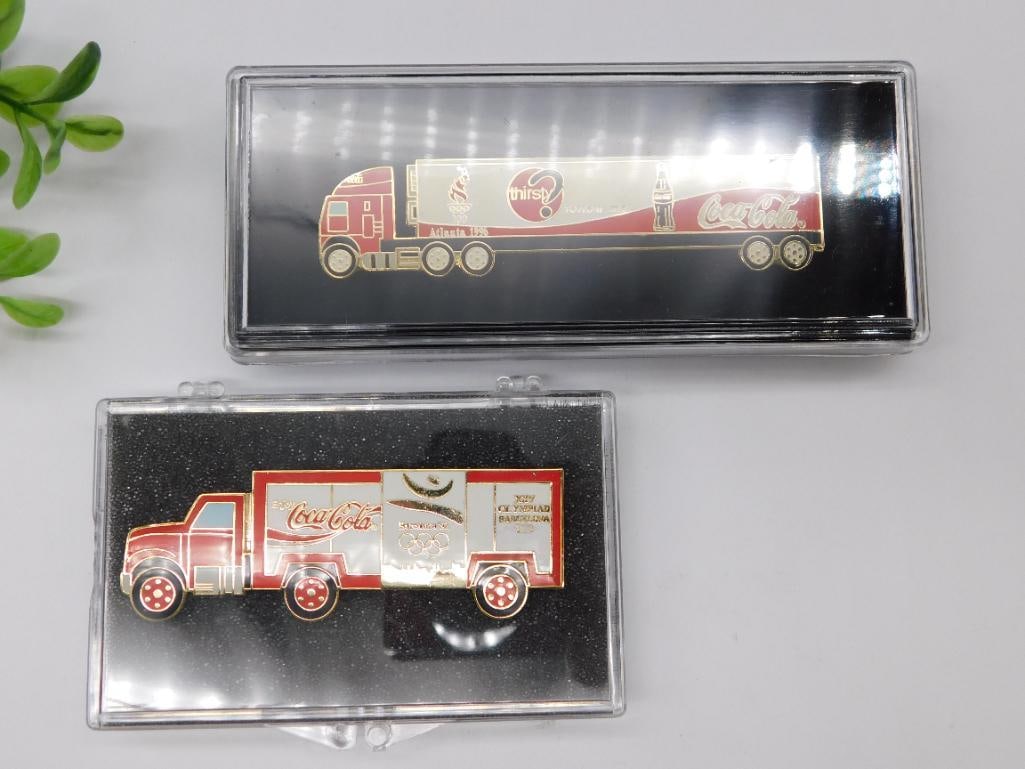 Coca-Cola Collectible Truck Pins: - Includes 2 Coca-Cola-themed collectible pins featuring truck designs. | - Pins are encased in separate clear display cases with black backgrounds. | - Feature red and white Coca-Cola branding detail