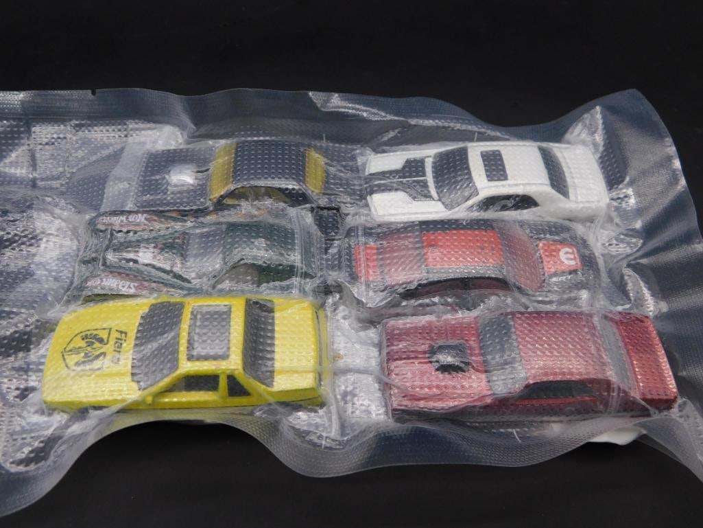 Lot of Six Hot Wheels Vehicles in Vacuum-Sealed Packaging: A collection of six Hot Wheels vehicles, all sealed in vacuum packaging for preservation. Includes various designs with markings on the bases indicating manufacturer and production details. Stamped wi