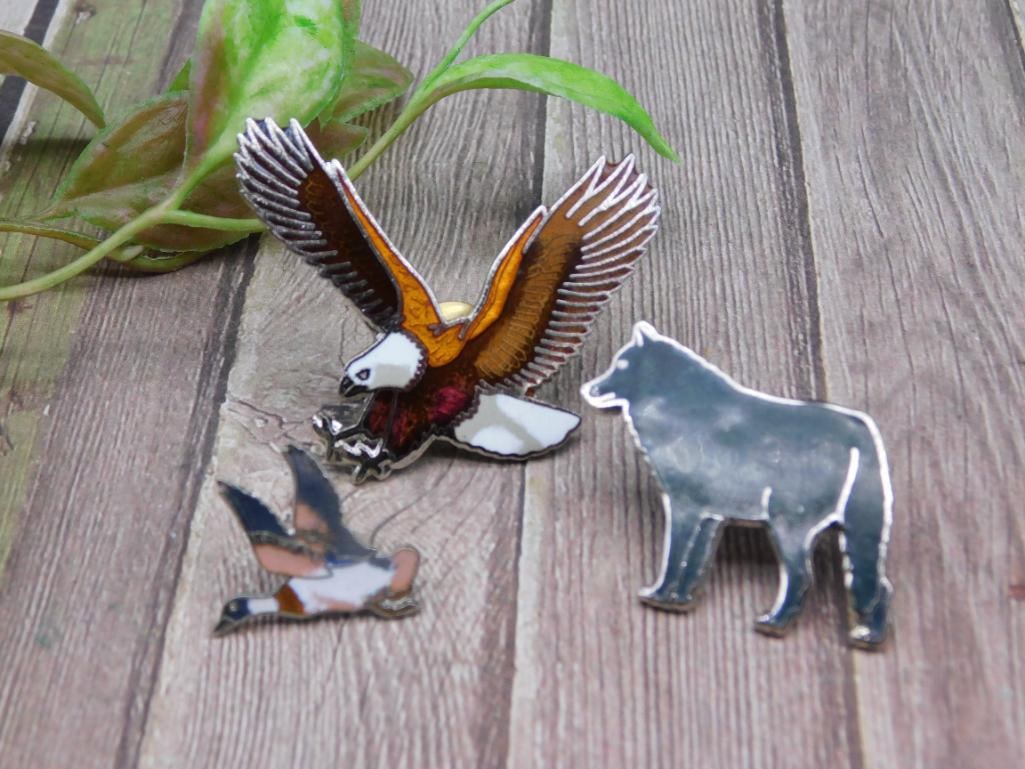 Set of Three Wildlife Themed Enamel Pins: This lot includes three wildlife-themed pins crafted in enamel. The set features an eagle mid-flight, a bear silhouette, and a smaller bird in flight. Each pin boasts detailed enamel work with vibrant