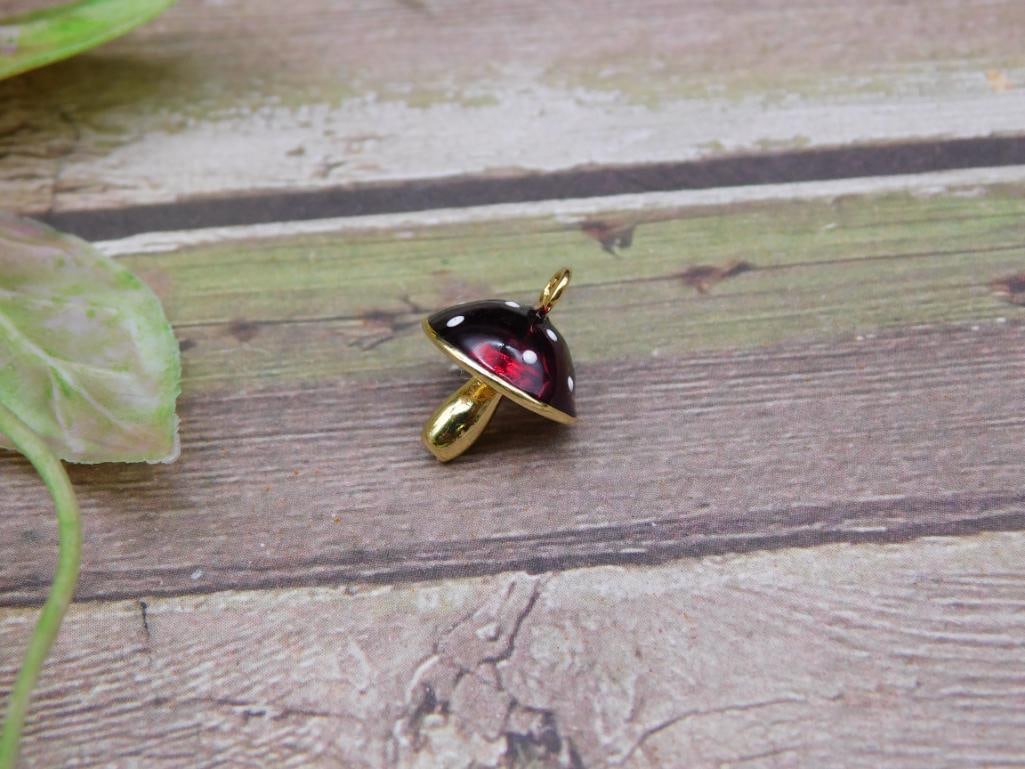 Gold-Tone Mushroom Pendant with Red and White Accents: Small mushroom-shaped pendant featuring a gold-tone body, a red cap with white accents, and a loop for attaching to a chain or bracelet. Compact size as shown in comparison to a U.S. quarter and ruler
